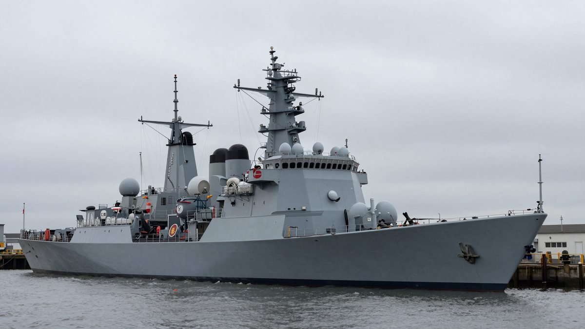A Royal Navy warship at anchor in a harbour under a moody grey sky