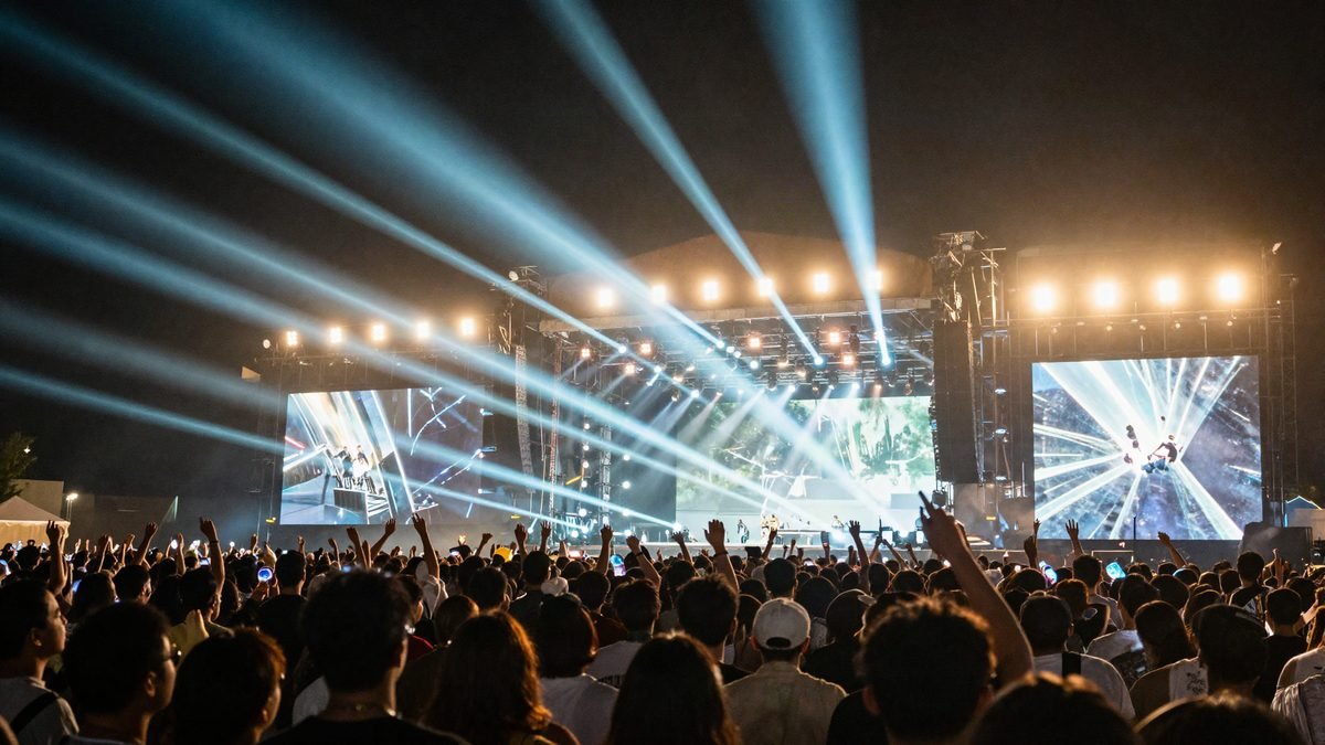 A festival stage at night with light beams and a silhouetted crowd