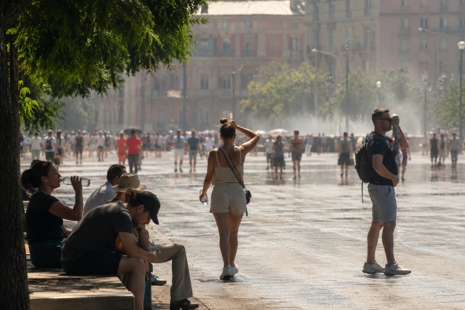A city street shimmering under intense summer heat with people seeking shade