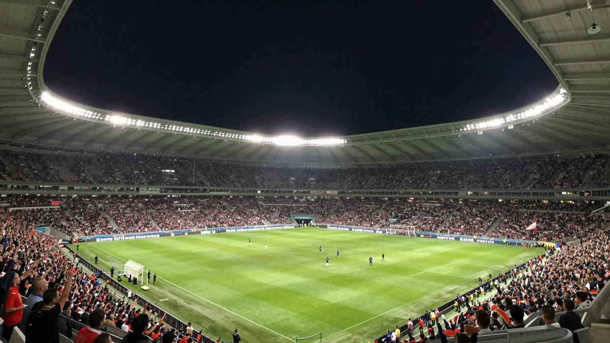 A packed football stadium at night filled with supporters after a match, floodlights blazing