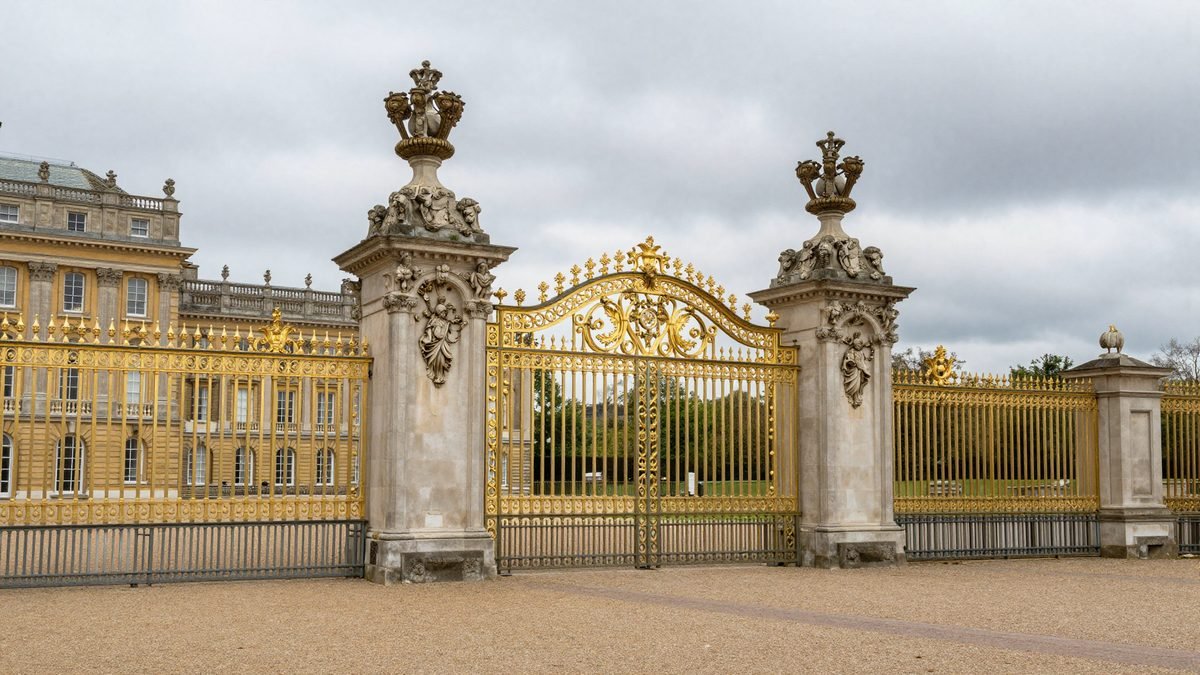 A grand historic royal residence behind ornate iron gates under a grey sky