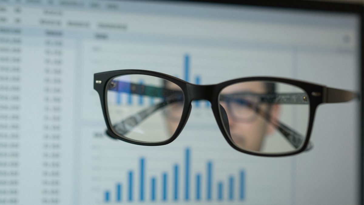 Rows of data on a computer screen reflected in a person's glasses in an office