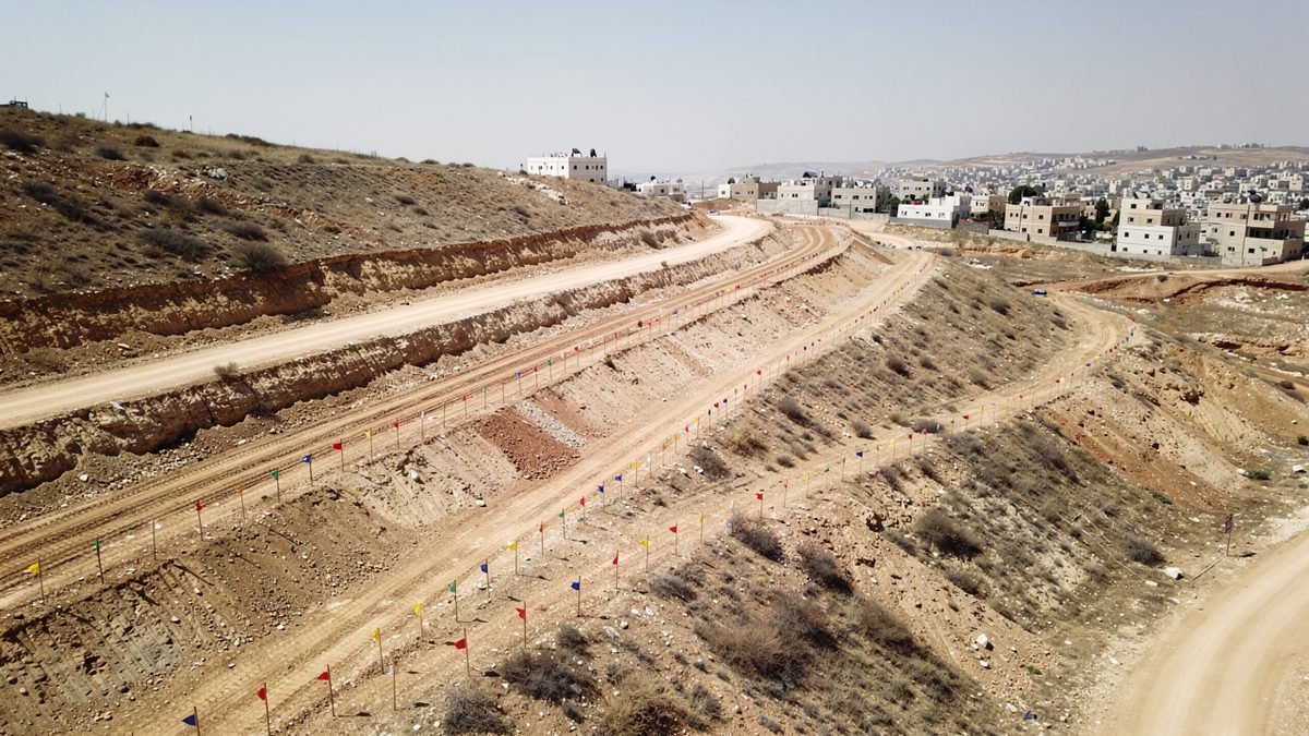 Aerial view of a hillside in the West Bank with construction earthworks and a town in the distance