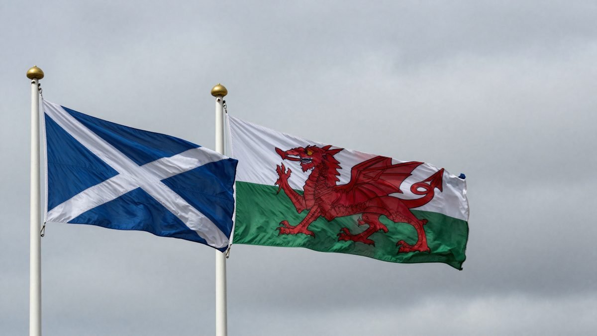 The flags of Scotland, Wales and the Union flag flying together on separate poles against a cloudy sky